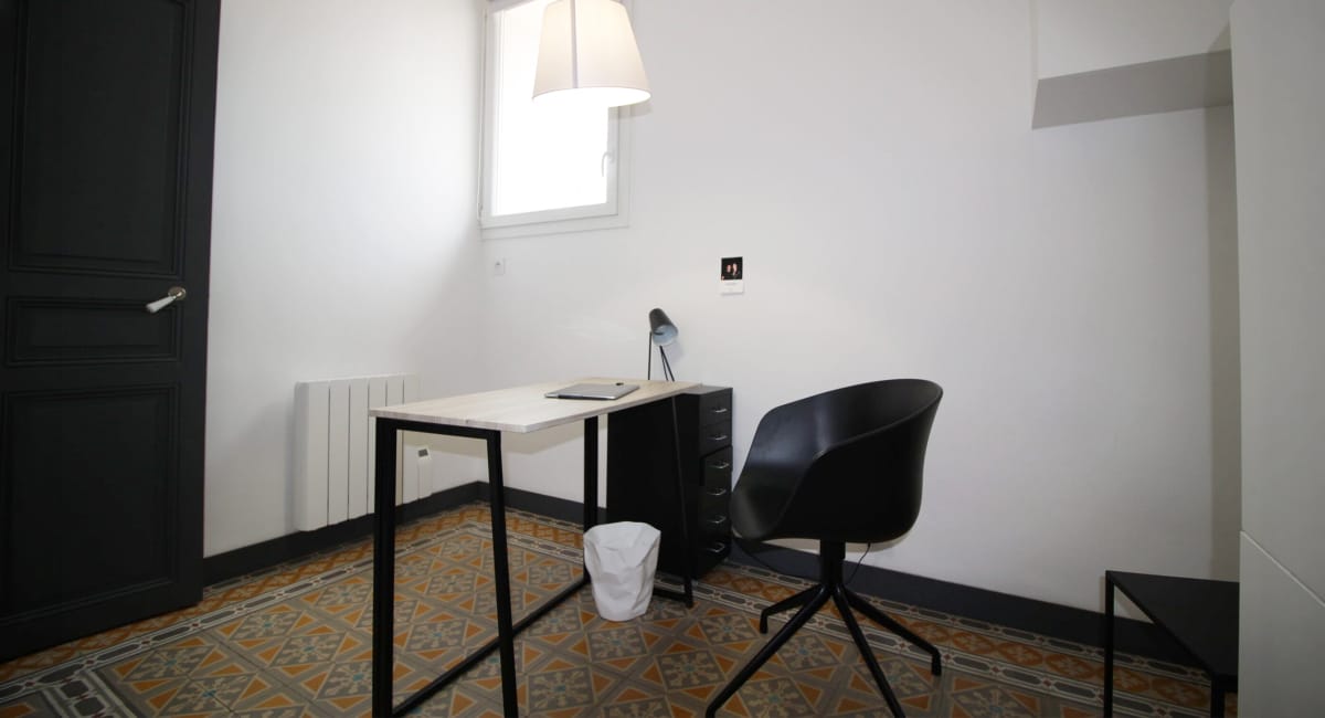 Une petite pièce avec un bureau, une chaise et un radiateur blanc.