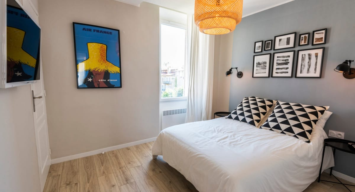 Une chambre cosy avec un lit blanc, un poster Air France et des décorations artistiques.