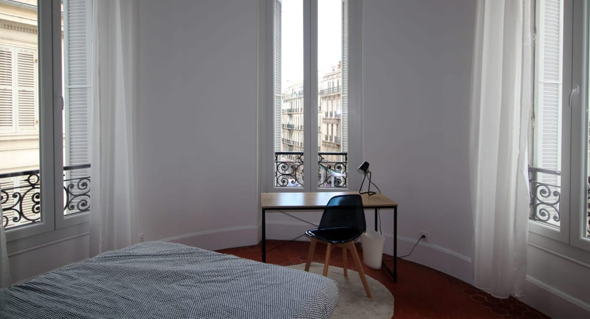 Une chambre lumineuse avec une vue sur Paris, un bureau et deux fenêtres décorées.