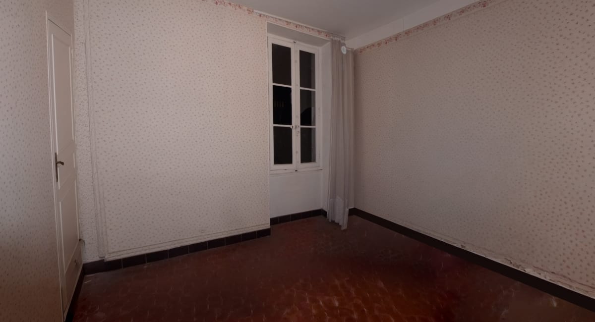 Une pièce sombre avec un papier peint floral et une fenêtre étroite.