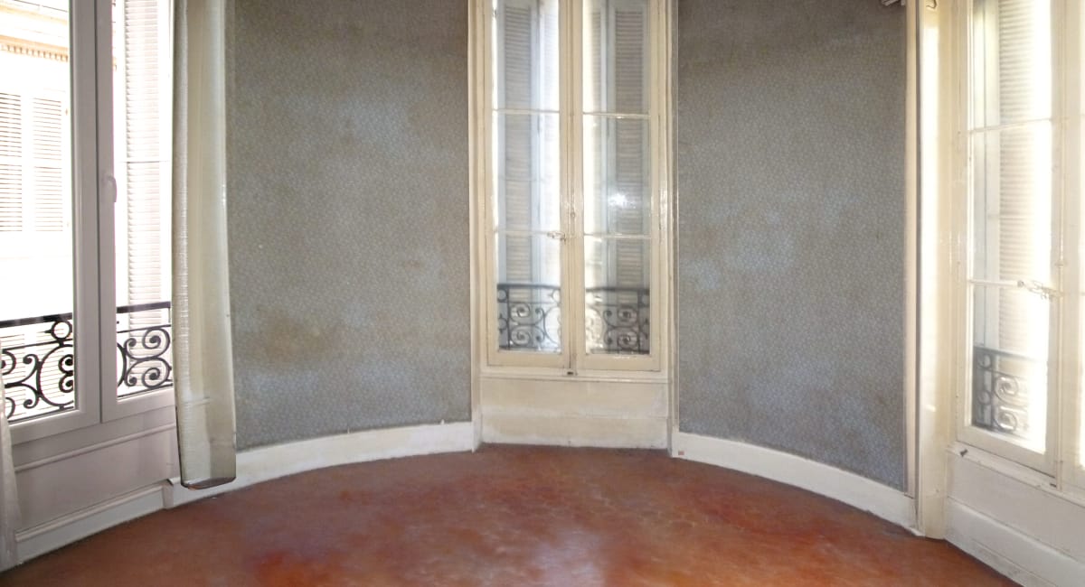 Une pièce d'intérieur avec des murs gris, des fenêtres et un sol en terre cuite.