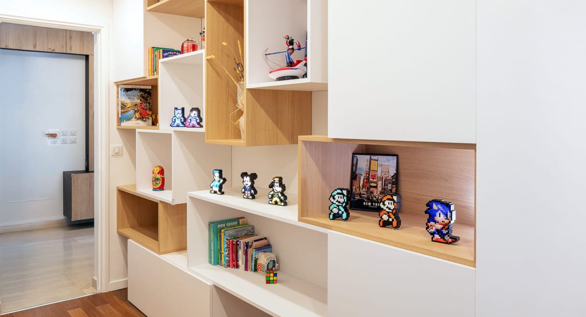 Une bibliothèque murale moderne et colorée, remplie de jouets et de livres, dans un intérieur cosy.