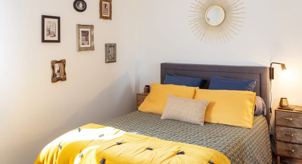 Une chambre cosy avec un lit jaune, des coussins bleus et des décorations murales.