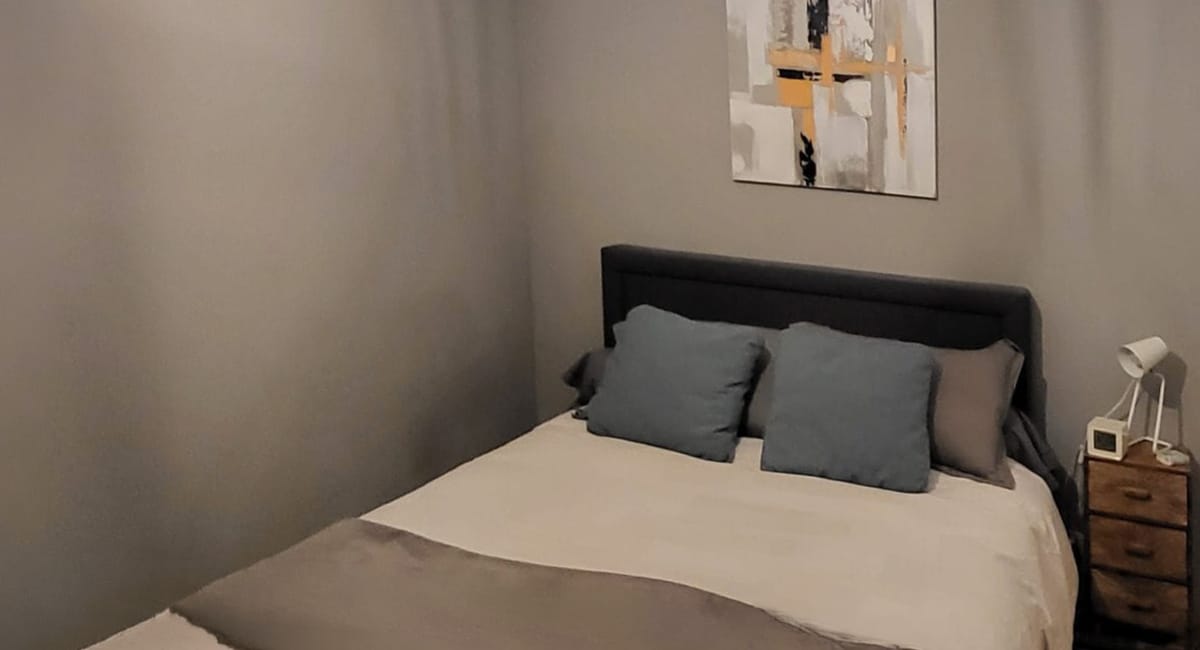 Une chambre cosy avec un lit douillet et des coussins gris.