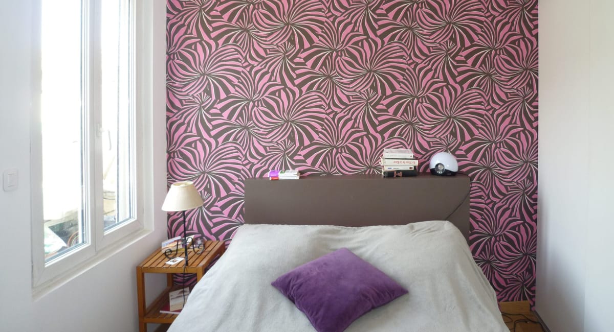 Une chambre cosy avec un papier peint rose et des motifs décoratifs, une tête de lit en bois et un lit confortable.