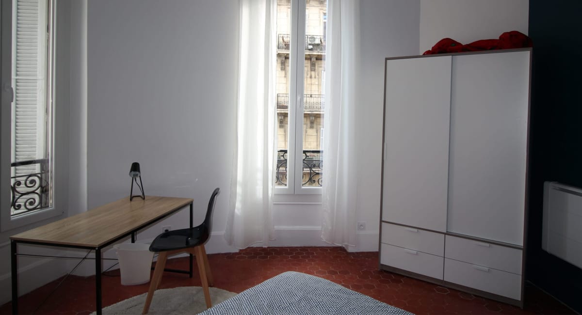 Une petite chambre avec un bureau, une armoire et une vue sur la rue.