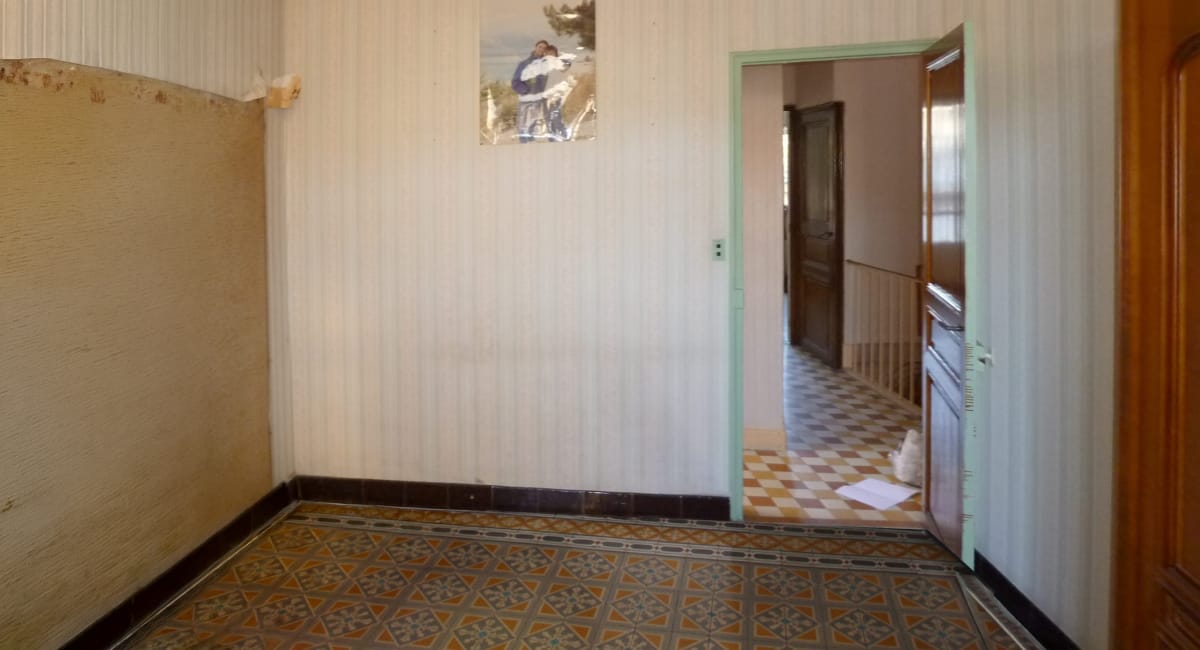 Un couloir ancien avec un papier peint beige et un motif de mariage.