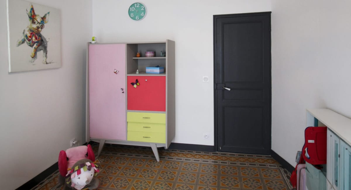 Une chambre d'enfant décorée avec un meuble rose, une porte noire et un sol carrelé.