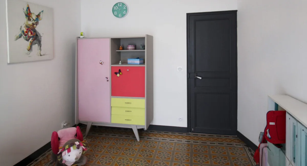 Une chambre d'enfant décorée avec un meuble rose, une porte noire et un sol carrelé.