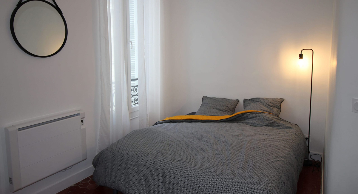 Chambre simple avec lit, rideaux et radiateur blanc.