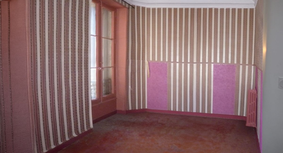 Une pièce avec un papier peint rayé beige et rose, une fenêtre et un meuble violet.