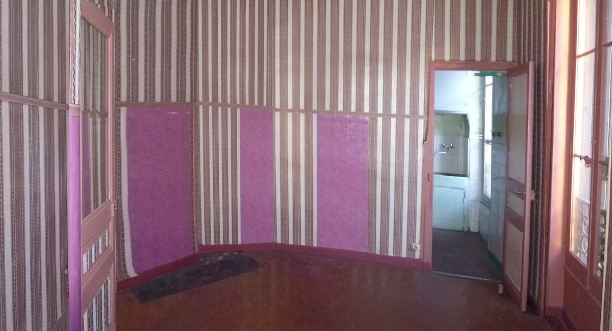 Piètre pièce avec un papier peint rayé et des couleurs vives, donnant sur un couloir.