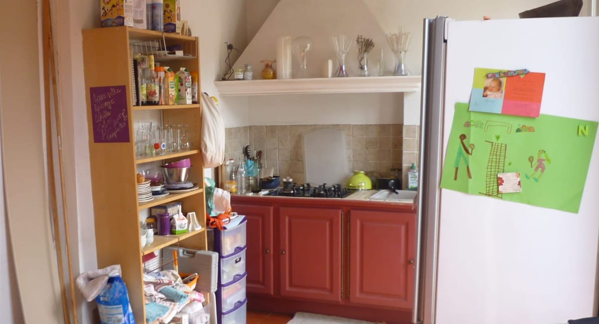 Cuisine familiale un peu encombrée avec des placards, un évier et un réfrigérateur.