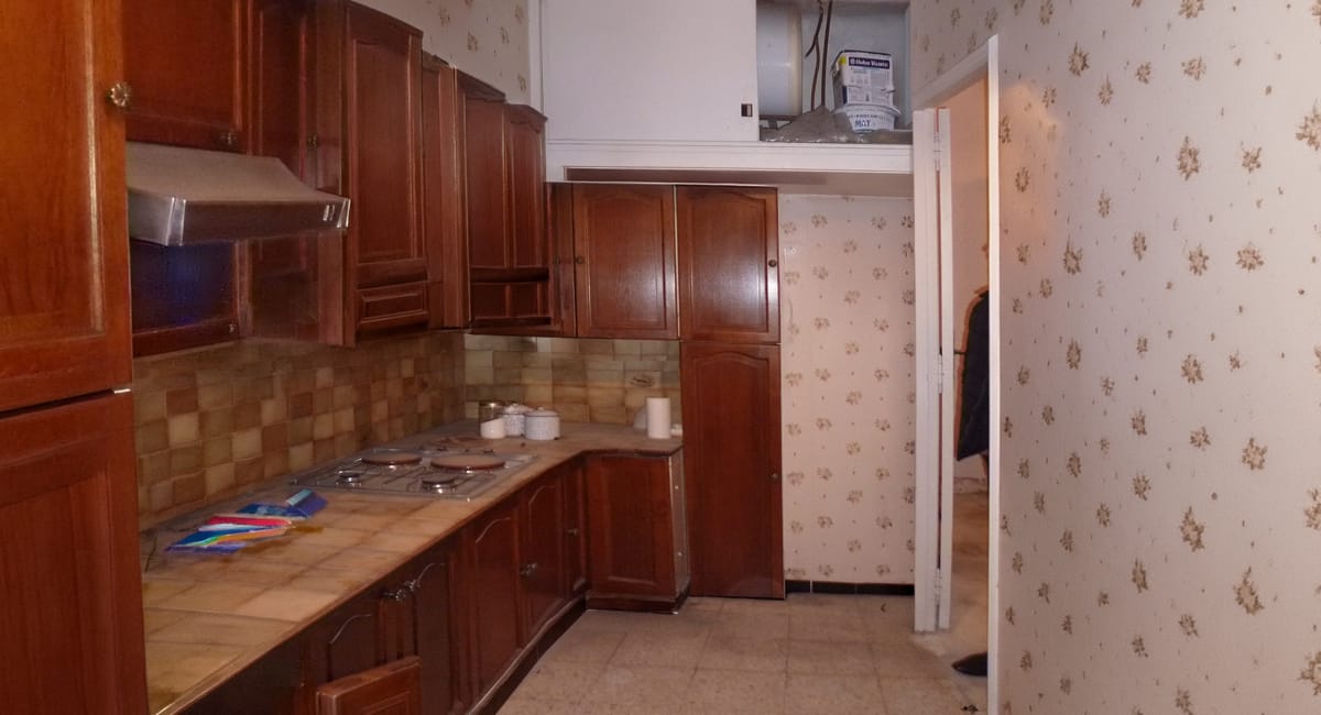 Cuisine avec armoires en bois sombre et papier peint fleuri, ambiance chaleureuse.