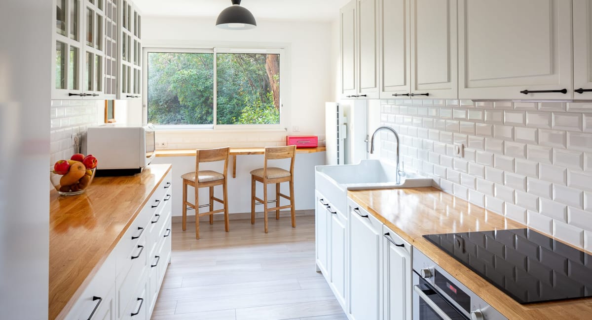 Cuisine moderne et lumineuse avec des armoires blanches, un plan de travail en bois et des carreaux de métro.