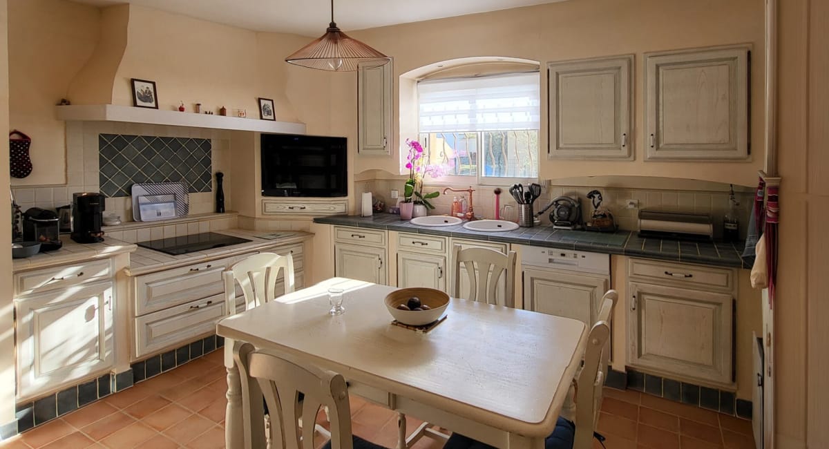 Cuisine chaleureuse et lumineuse avec une table et des armoires blanches.