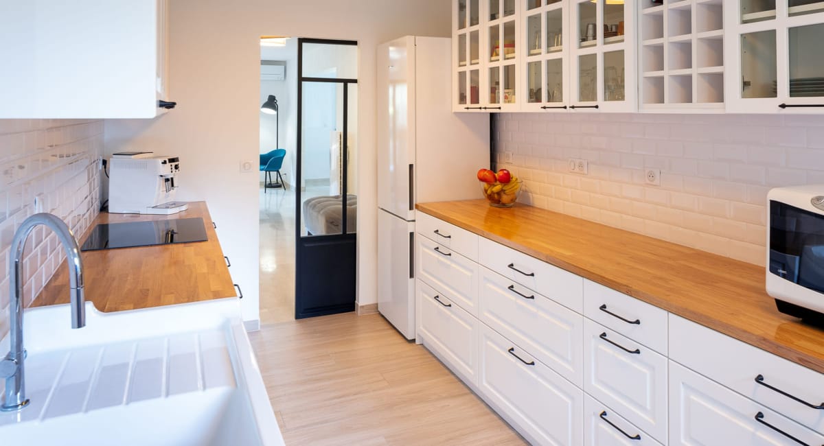 Cuisine moderne et lumineuse avec des armoires blanches et un plan de travail en bois.