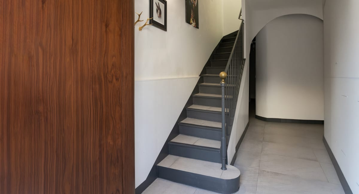 Des escaliers gris mènent à un escalier en arc, dans un couloir élégant.
