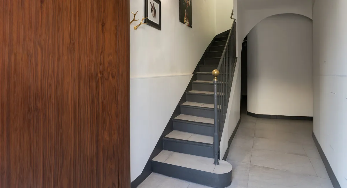 Des escaliers gris mènent à un escalier en arc, dans un couloir élégant.