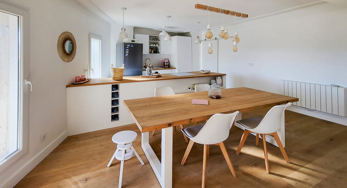 Une cuisine-salon moderne et lumineuse avec une grande table à manger et des chaises blanches.