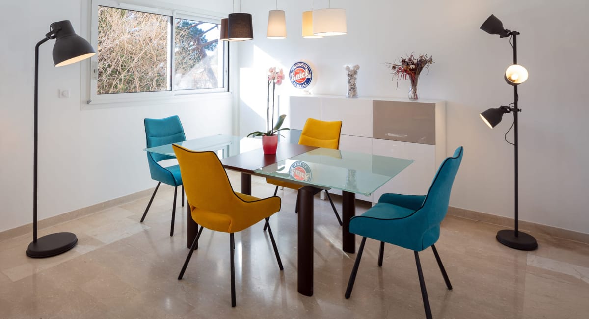 Une salle à manger moderne avec une table en verre et des chaises colorées.