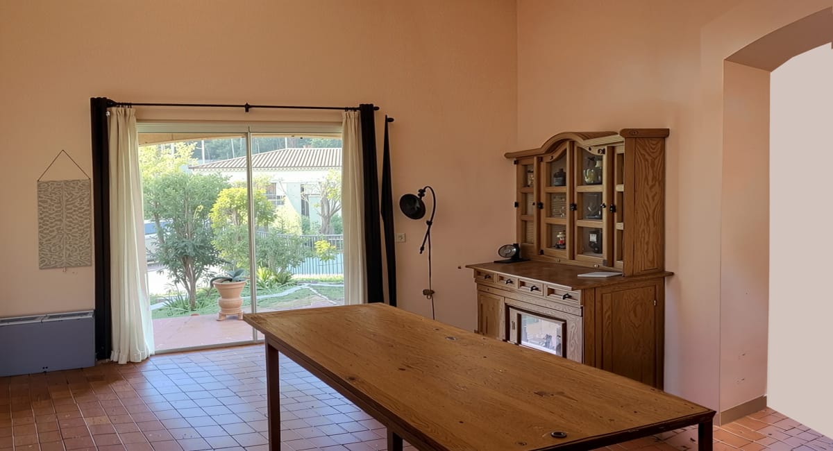 Intérieur d'une pièce avec une grande table, une armoire et une vue sur le jardin.