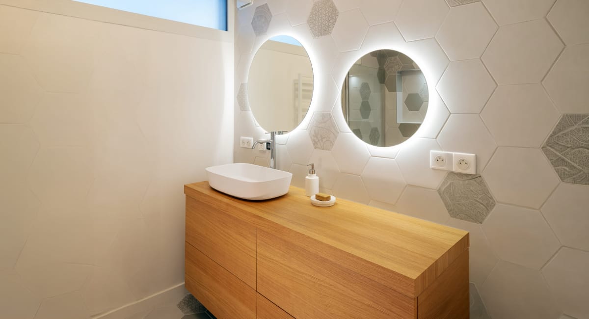 Salle de bain moderne avec un meuble vasque en bois et deux miroirs lumineux.