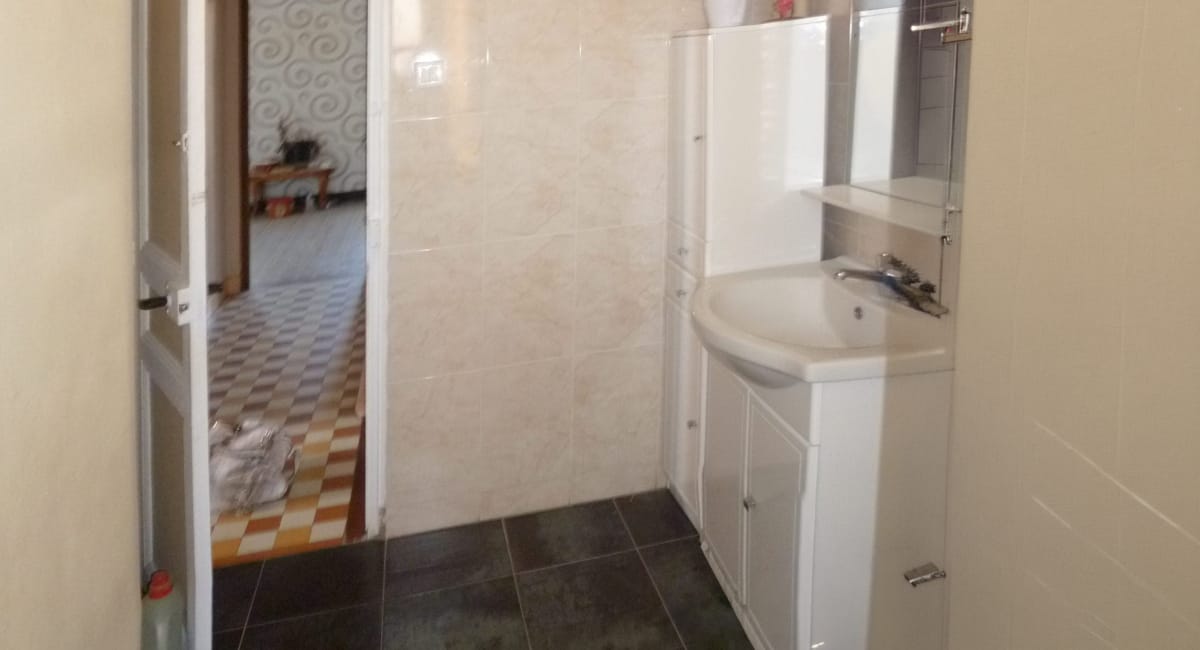 Salle de bain simple avec lavabo et carrelage, vue sur un couloir.