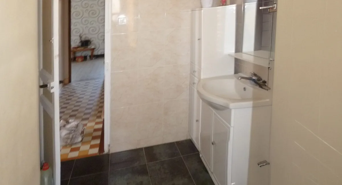 Salle de bain simple avec lavabo et carrelage, vue sur un couloir.