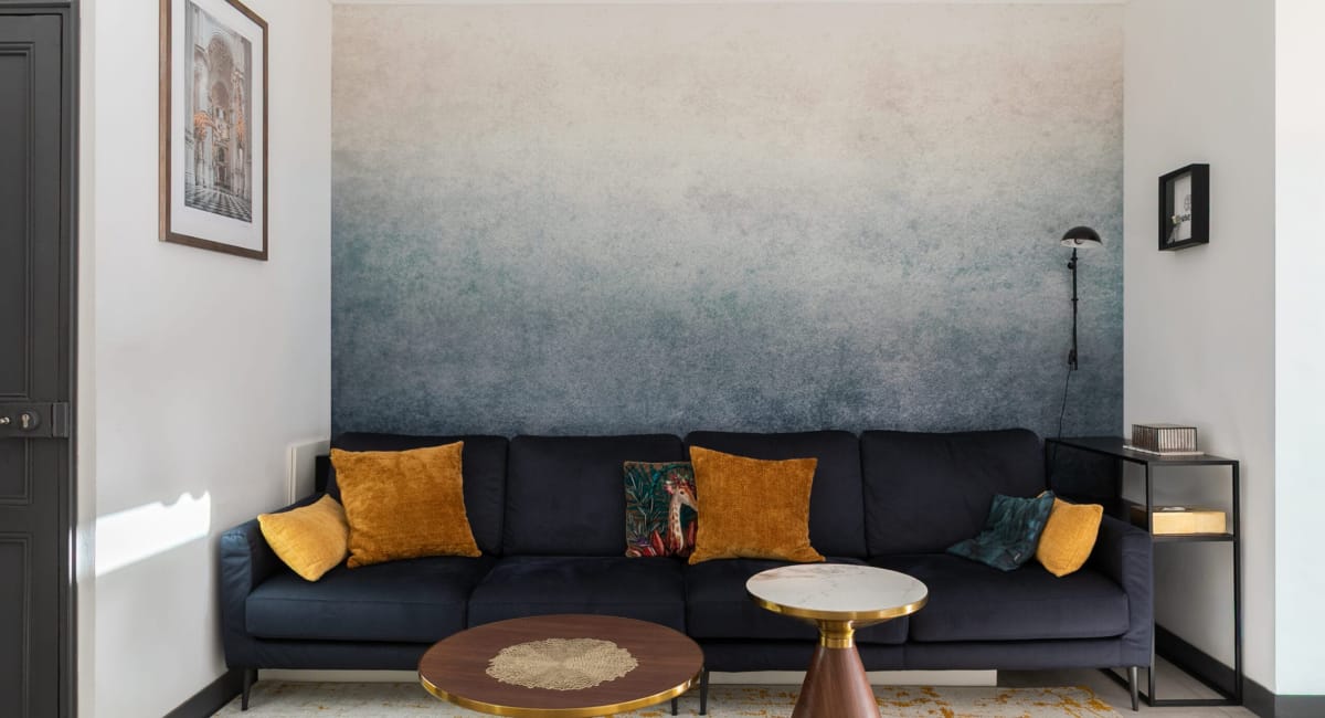 Un salon moderne avec un canapé bleu foncé, des coussins dorés et une décoration murale artistique.