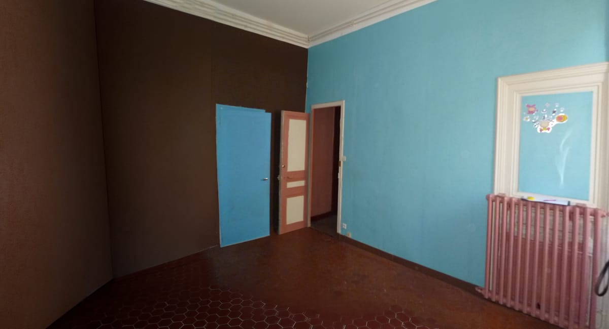 Une pièce sombre avec des murs marron et un angle bleu, décorée d'une fenêtre et d'un radiateur.
