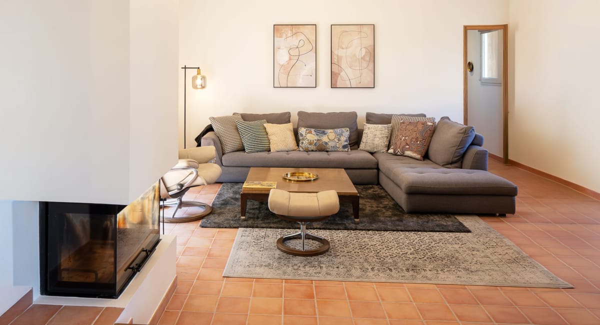 Salon cosy avec canapé d'angle gris, cheminée et tapis traditionnel.