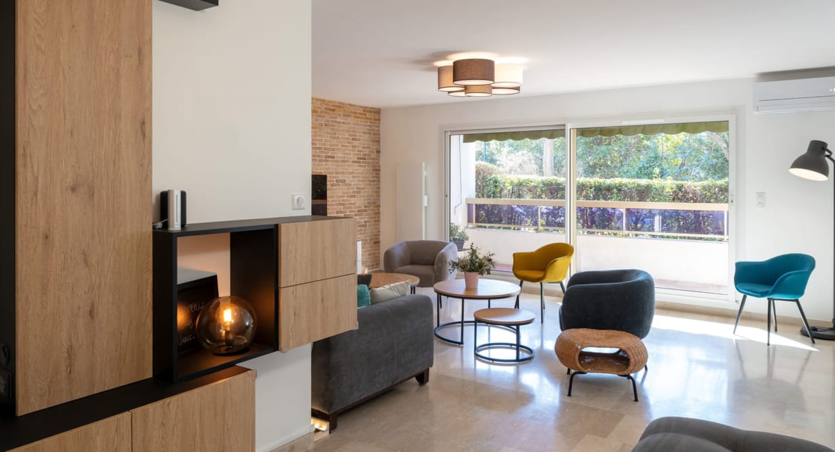 Salon moderne et lumineux avec canapé gris, fauteuils colorés et vue sur jardin.