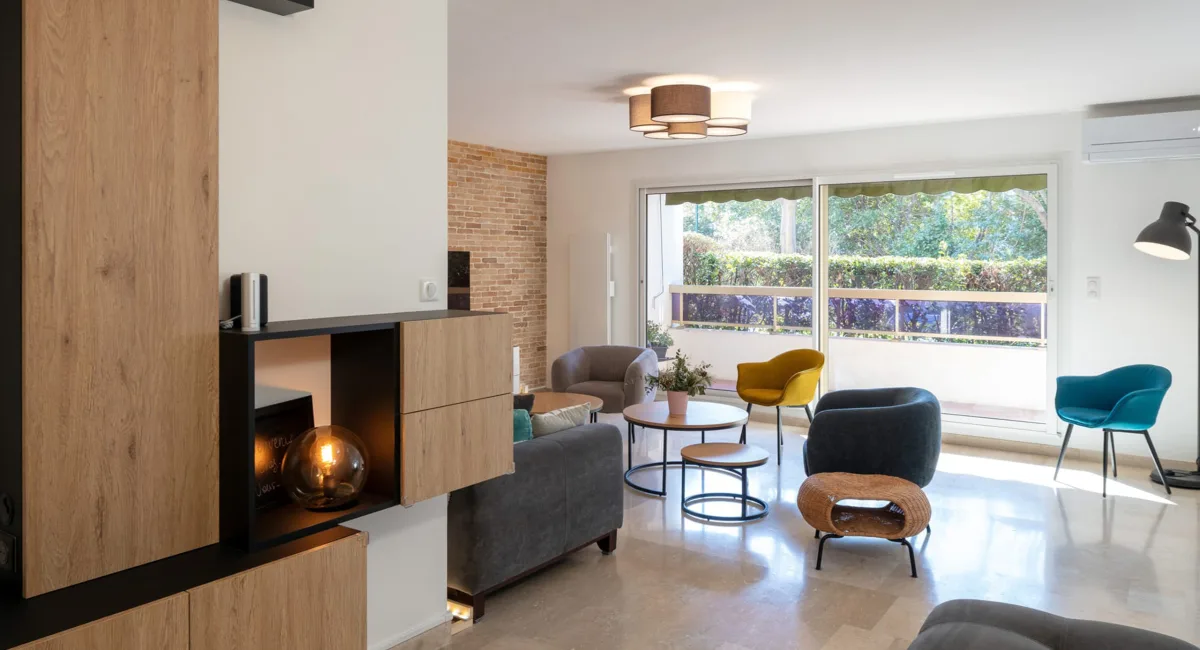 Salon moderne et lumineux avec canapé gris, fauteuils colorés et vue sur jardin.