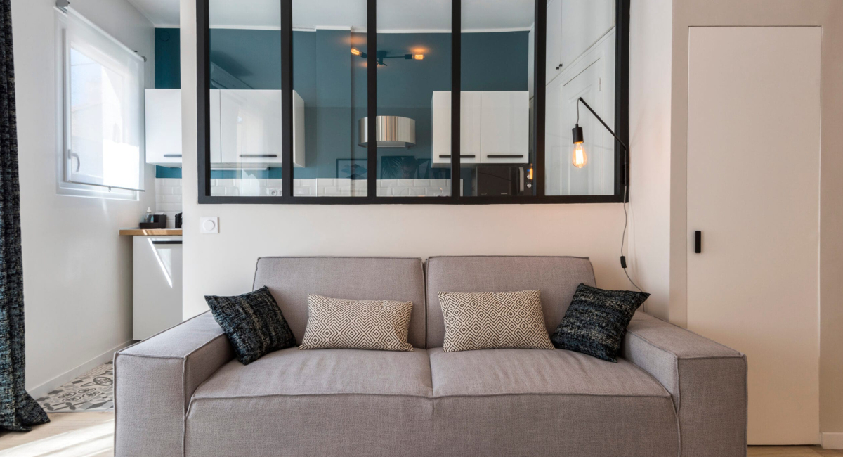 Un salon cosy avec un canapé gris et des coussins décoratifs devant une cloisonnette en verre.