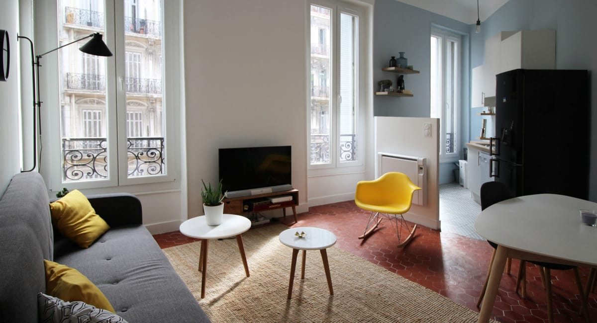 Intérieur d'un appartement moderne et lumineux avec canapé, télé et cuisine ouverte.