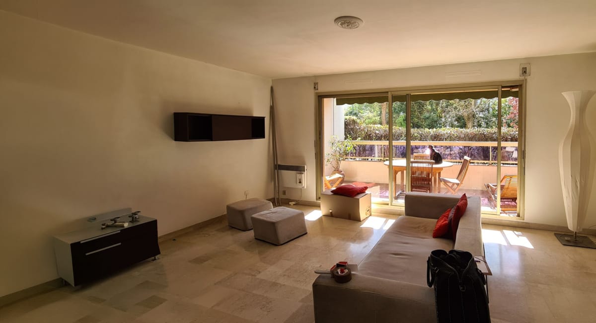 Salon lumineux avec canapé gris, télévision et vue sur un balcon.