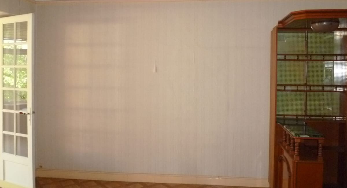 Mur beige simple avec un clou et une étagère en bois à côté.