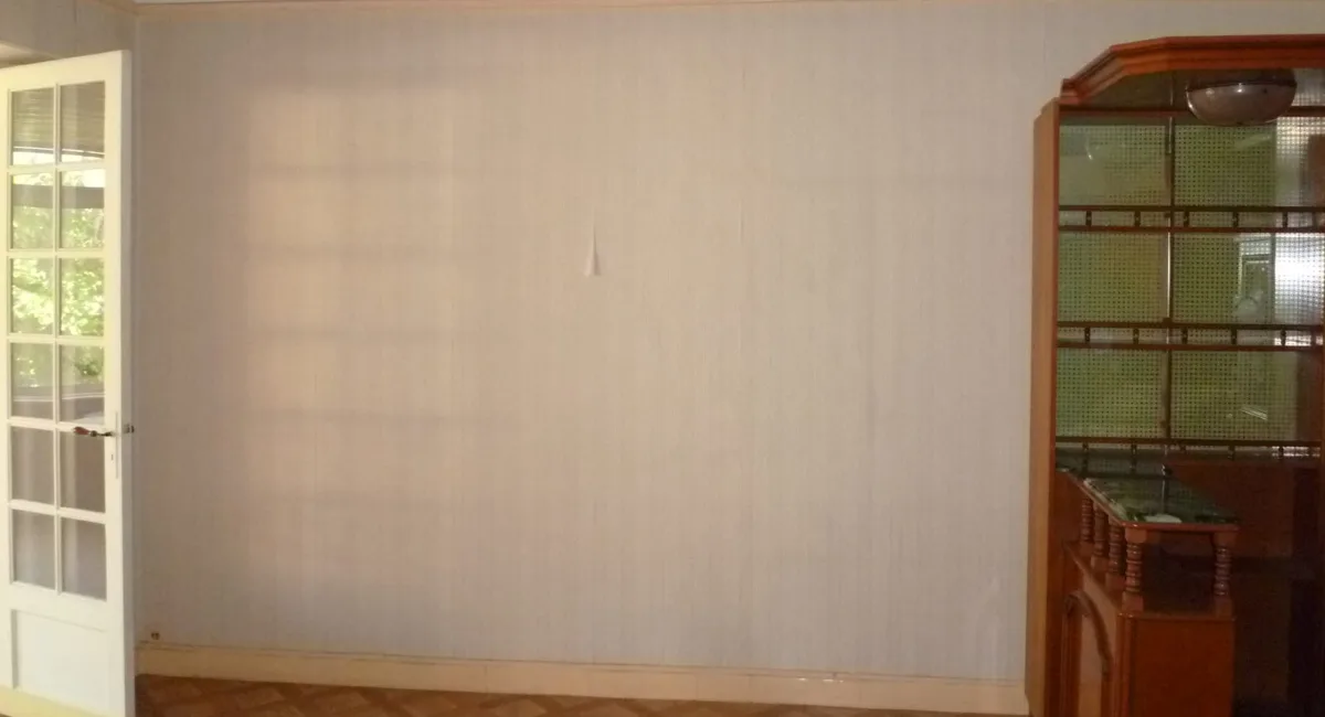Mur beige simple avec un clou et une étagère en bois à côté.