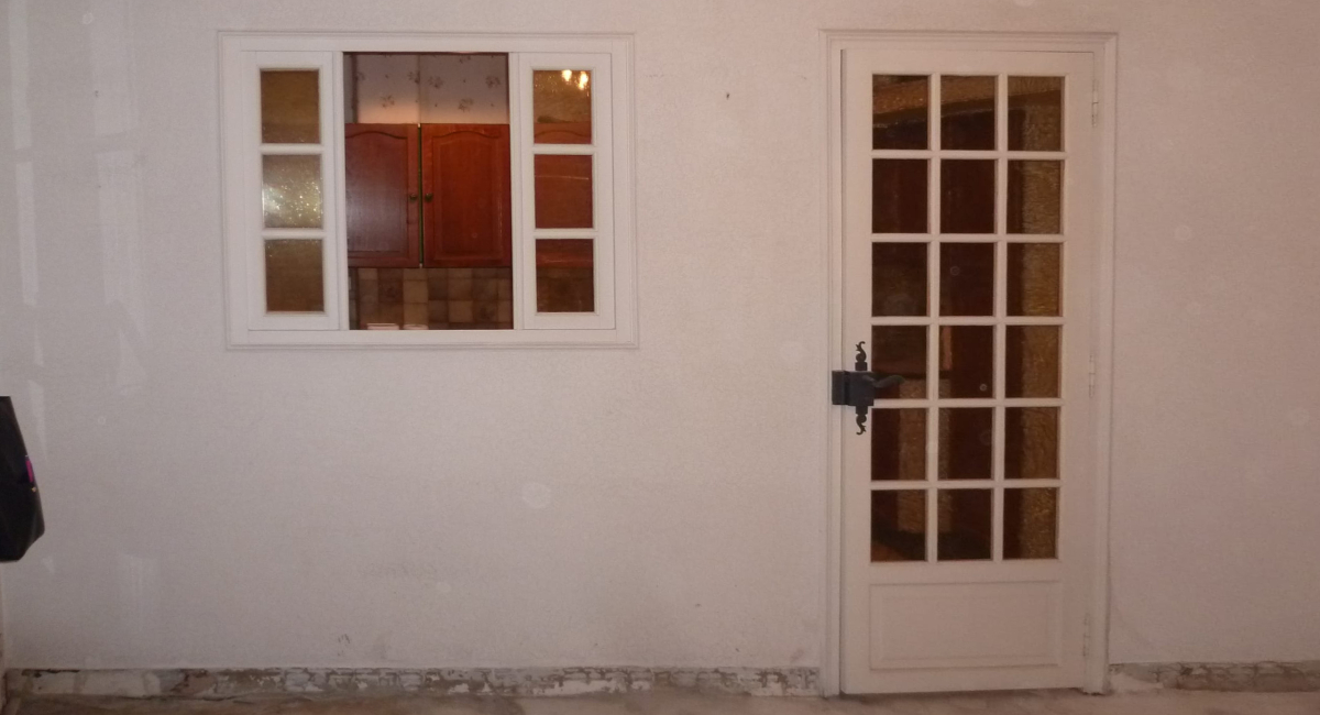 Mur blanc avec une fenêtre et une porte en rez-de-chaussée.
