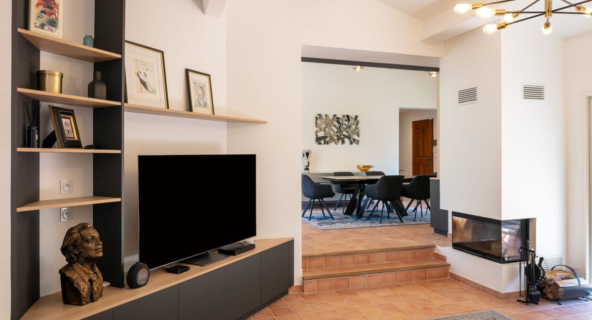 Intérieur moderne avec étagère, téléviseur et accès à un salon lumineux.