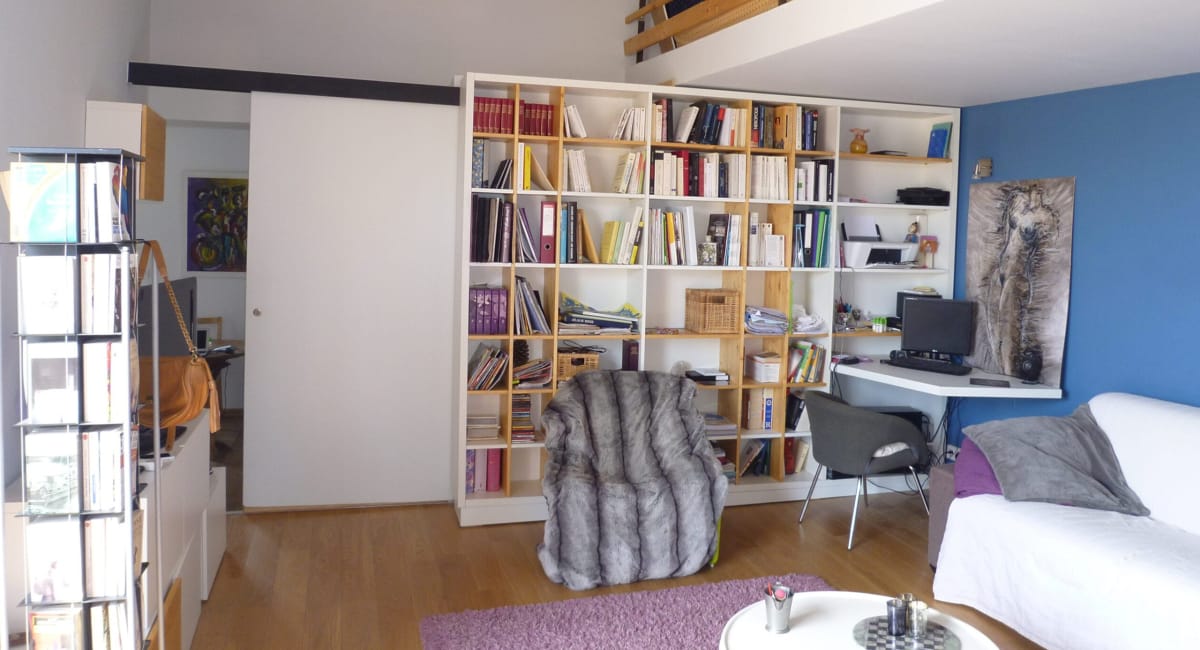 Une bibliothèque blanche encombrée de livres et un bureau dans un salon chaleureux.