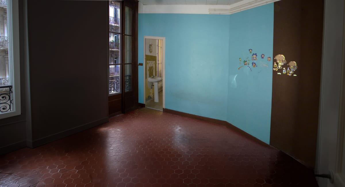 Un couloir d'une maison ancienne avec un sol en carreaux hexagonaux et des murs colorés.
