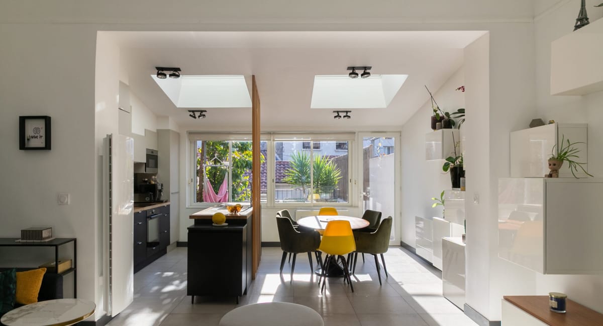 Intérieur lumineux d'une salle à manger avec une cuisine ouverte et des fenêtres donnant sur la rue.