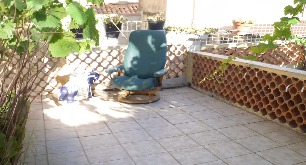 Un fauteuil bleu sur un balcon avec des plantes et un mur en briques.