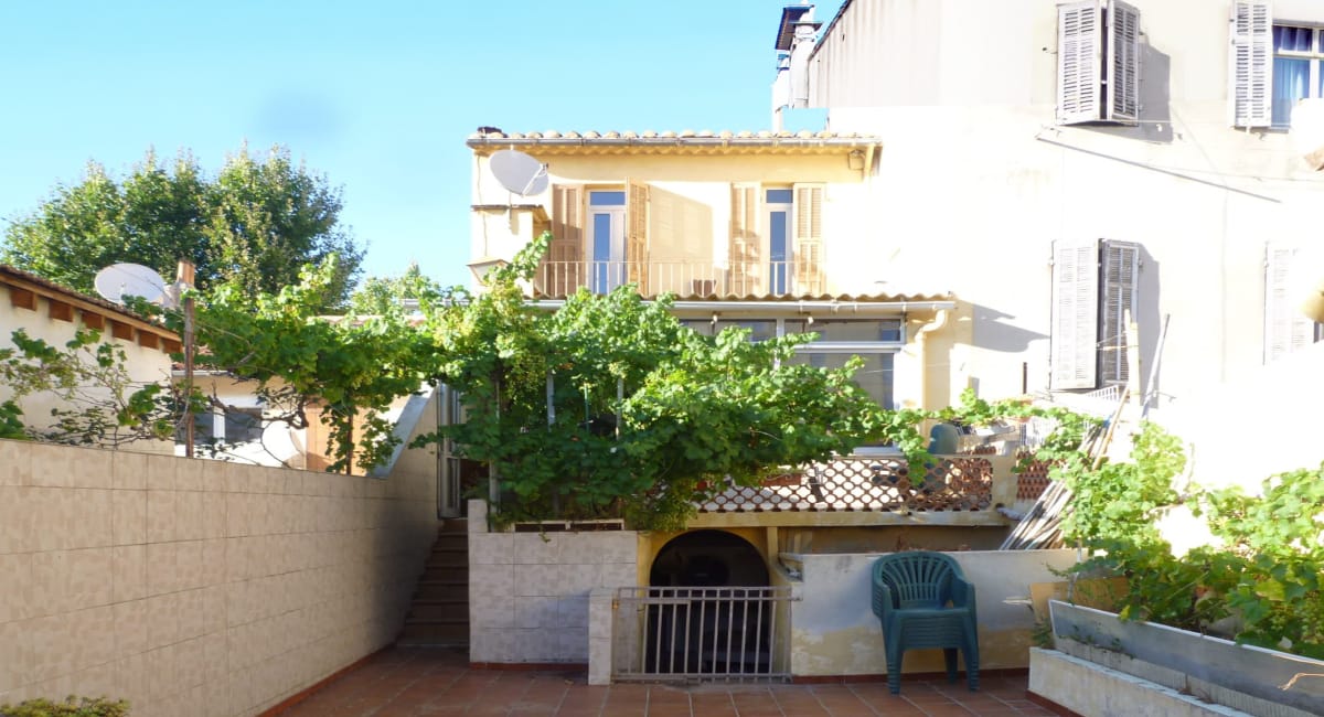 Vue arrière d'une maison de ville avec un jardin et une petite terrasse.