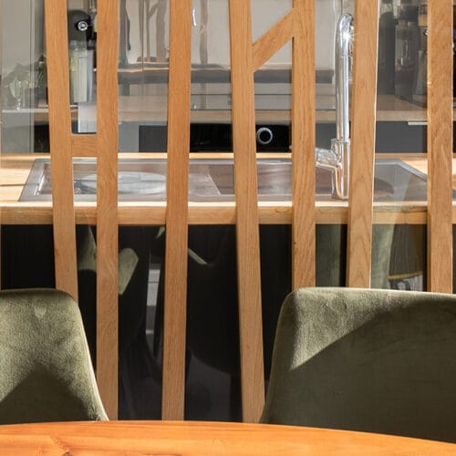 Un comptoir en bois avec une séparation en bois et deux chaises vertes dans une cuisine moderne.