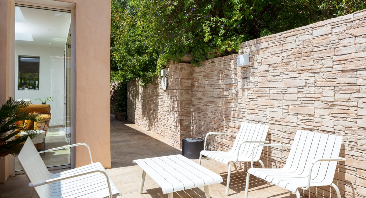 Un charmant patio avec des chaises blanches et un mur en pierre naturelle.