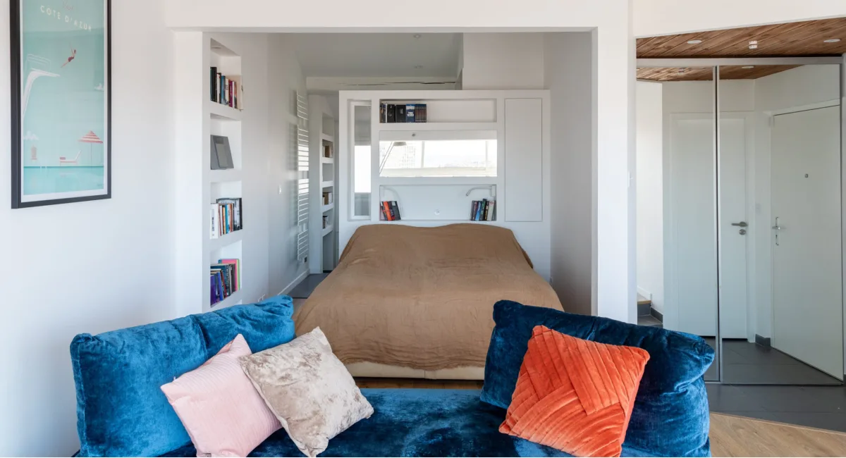 Une chambre cosy avec un lit surélevé, des coussins bleus et des étagères blanches.