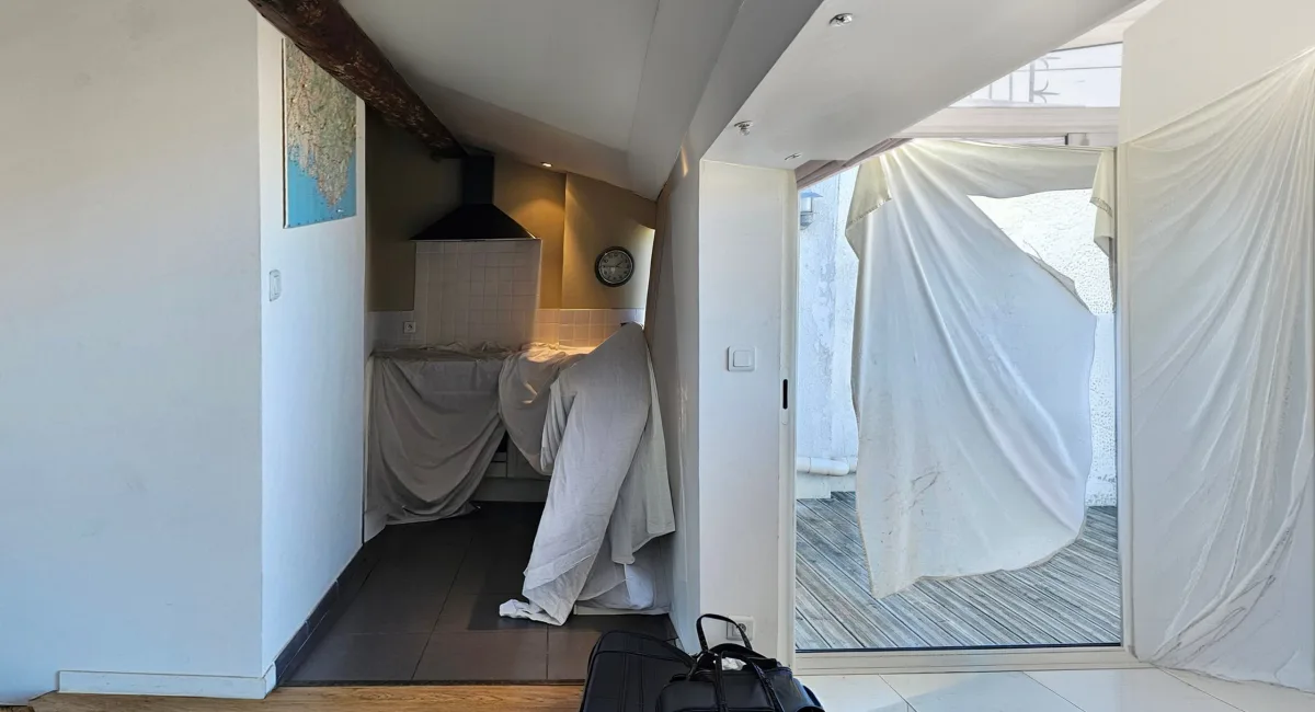 Cuisine d'un appartement ancien avec rideaux blancs et vue sur l'extérieur.